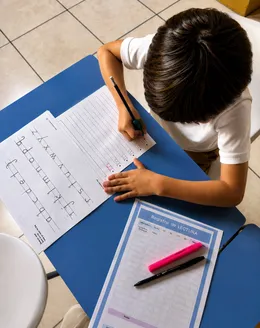 Vista desde arriba de un niño practicando caligrafía junto a su registro de lectura.