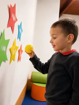 Niño coloca una pelota amarilla sobre estrellas de colores pegadas en la pared.