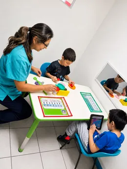 Terapeuta acompaña a dos niños en una sesión con tableros de comunicación por pictogramas.