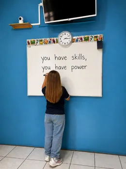 Niña escribe "you have skills, you have power" en la pizarra del aula.