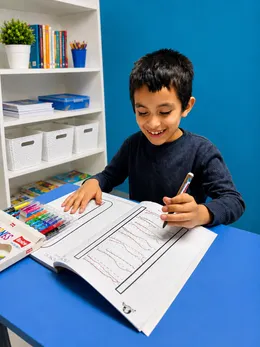 Niño traza líneas en un cuaderno de grafomotricidad con marcadores de colores.